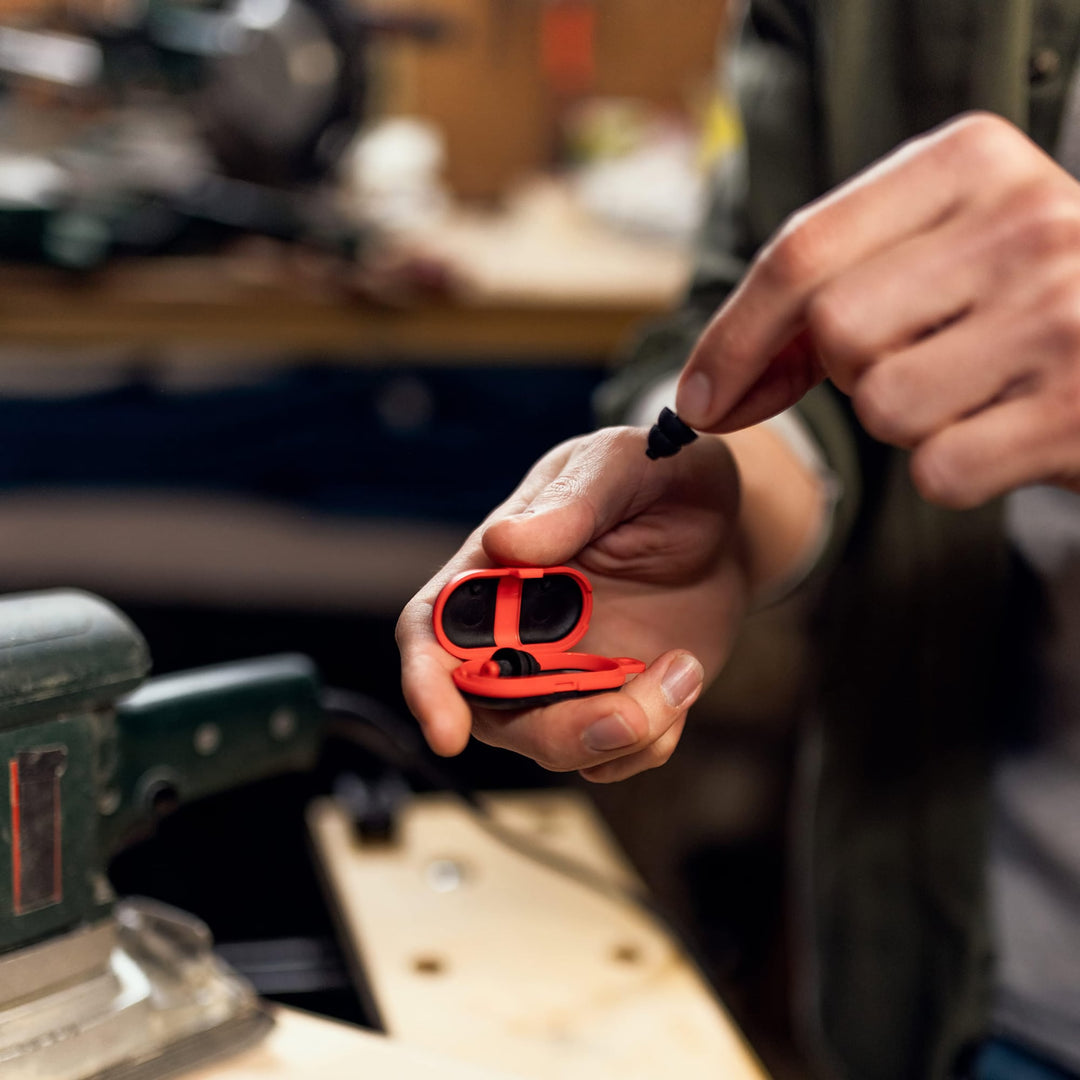 Person taking Alpine WorkSafe earplug from red case in a workshop, highlighting portability and use in noisy environments