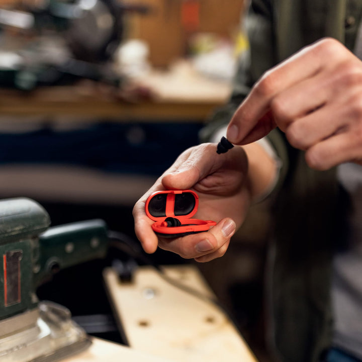 Person taking Alpine WorkSafe earplug from red case in a workshop, highlighting portability and use in noisy environments