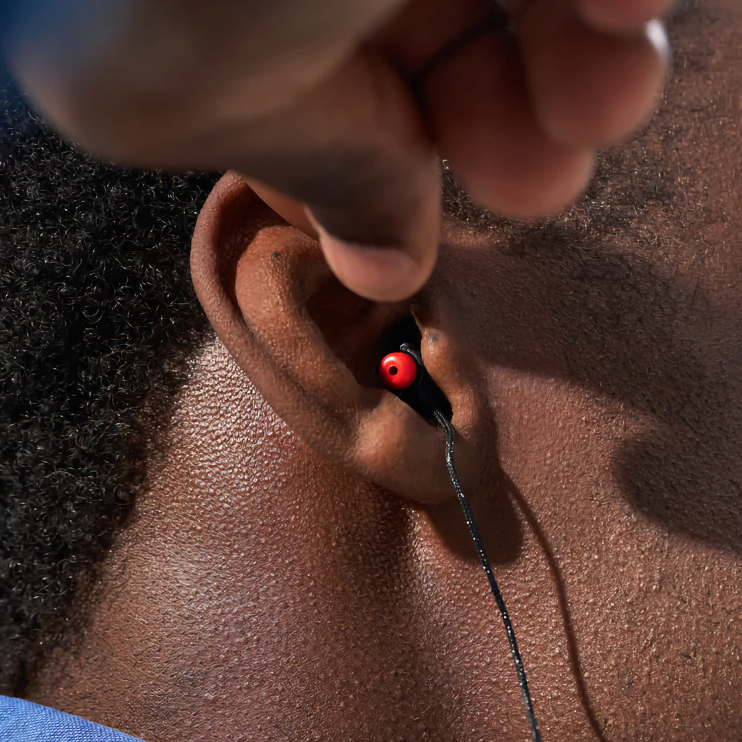 Close-up of Alpine WorkSafe earplug being inserted into ear, showing proper fit and red acoustic filter tip