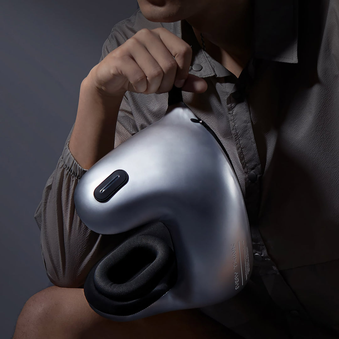 Person holding EVERYTHINK E2-X travel neck pillow by strap, metallic silver design shown clearly