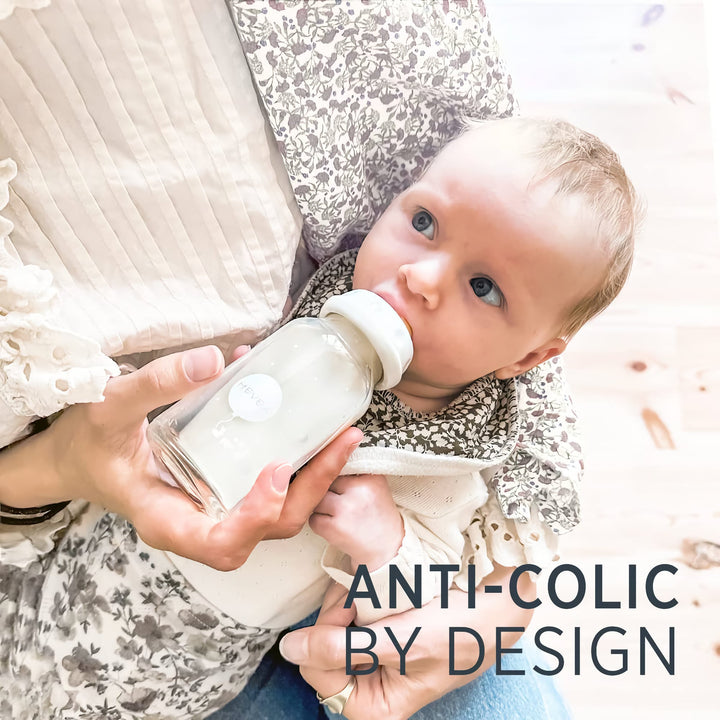 Baby drinking from a HEVEA glass bottle with a natural rubber nipple, designed with an anti-colic valve for a comfortable feeding experience.