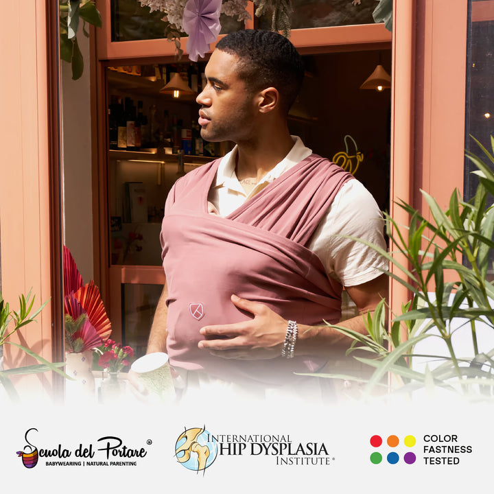Man wearing Koala Babycare Koala Cuddle Band 2 in earth red, carrying a baby outdoors with soft, ergonomic fabric for comfort.