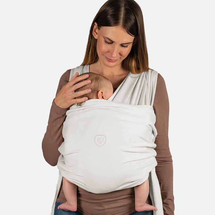 Mother wearing the Koala Babycare Koala Cuddle Band 2 baby sling carrier in light gray, holding a baby close for hands-free comfort and support.