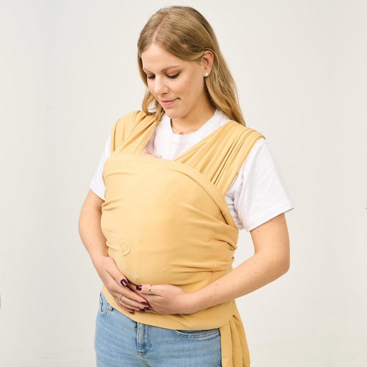 Woman wearing Koala Cuddle Band 2 in mustard color while gently holding baby