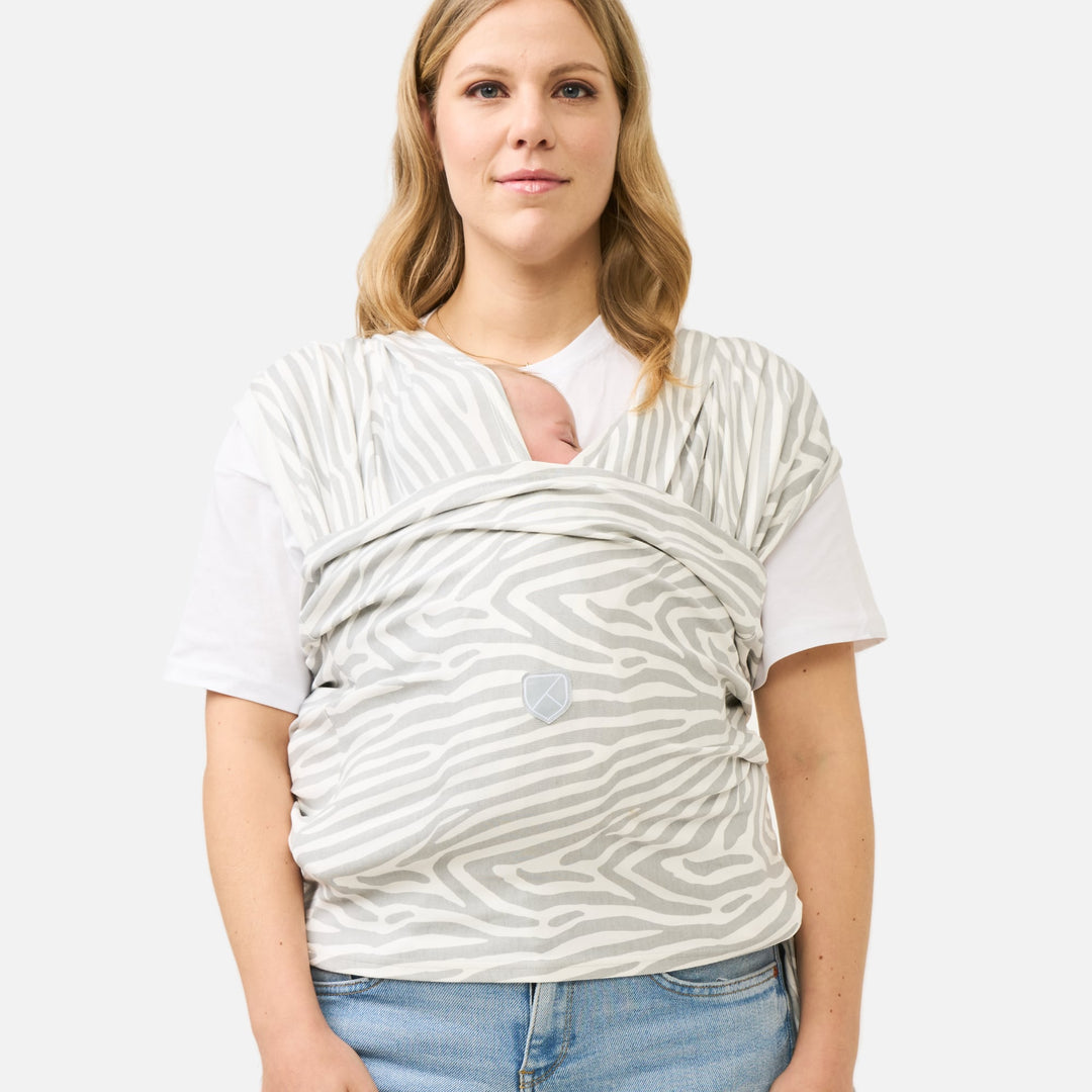 Mother wearing the Koala Cuddle Band 2 baby sling carrier in tiger-print gray, securely holding her baby in a comfortable and ergonomic position.
