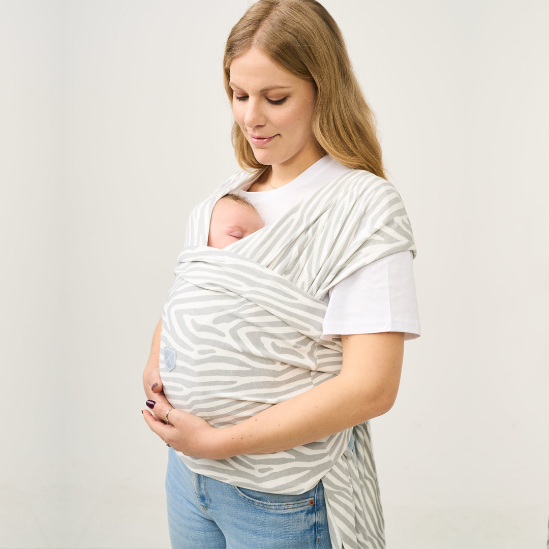 Mother wearing the Koala Cuddle Band 2 baby wrap carrier in tiger-print gray, gently cradling her sleeping baby in a secure and ergonomic position.