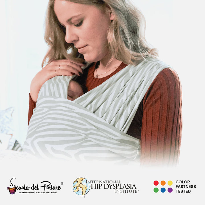 Mother wearing the Koala Cuddle Band 2 baby sling carrier in tiger-print gray, gently holding her sleeping baby. Certified for hip health and color fastness.