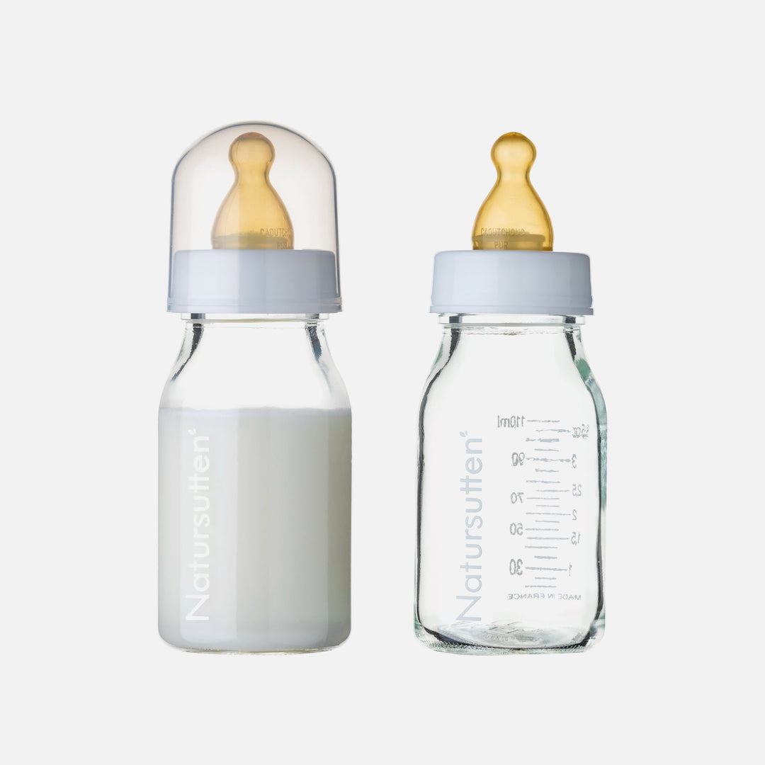 Natursutten 110ml glass baby bottles shown with natural rubber nipples, one filled with milk and one empty with clear volume markings