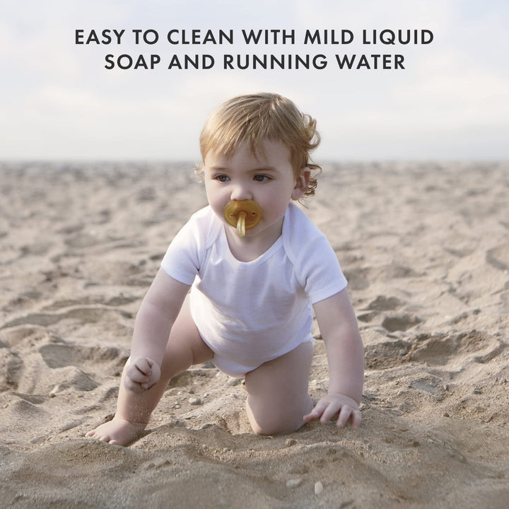 Baby using Natursutten Natural Rubber Pacifier while crawling on the beach, highlighting its easy-to-clean design with mild soap and water.