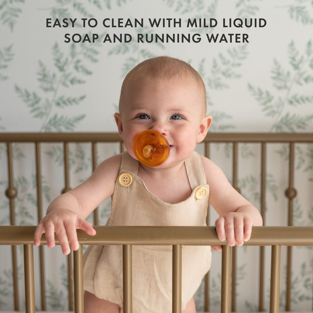 Smiling baby in crib with Natursutten pacifier, easy to clean with mild soap and water