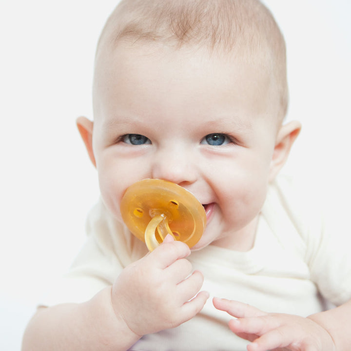 Close-up of smiling baby holding Natursutten natural rubber orthodontic pacifier