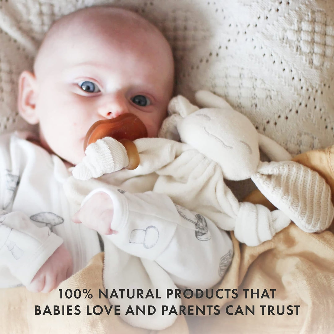 Baby holding Natursutten PaciPixy comforter with attached natural rubber pacifier, safe and trusted by parents