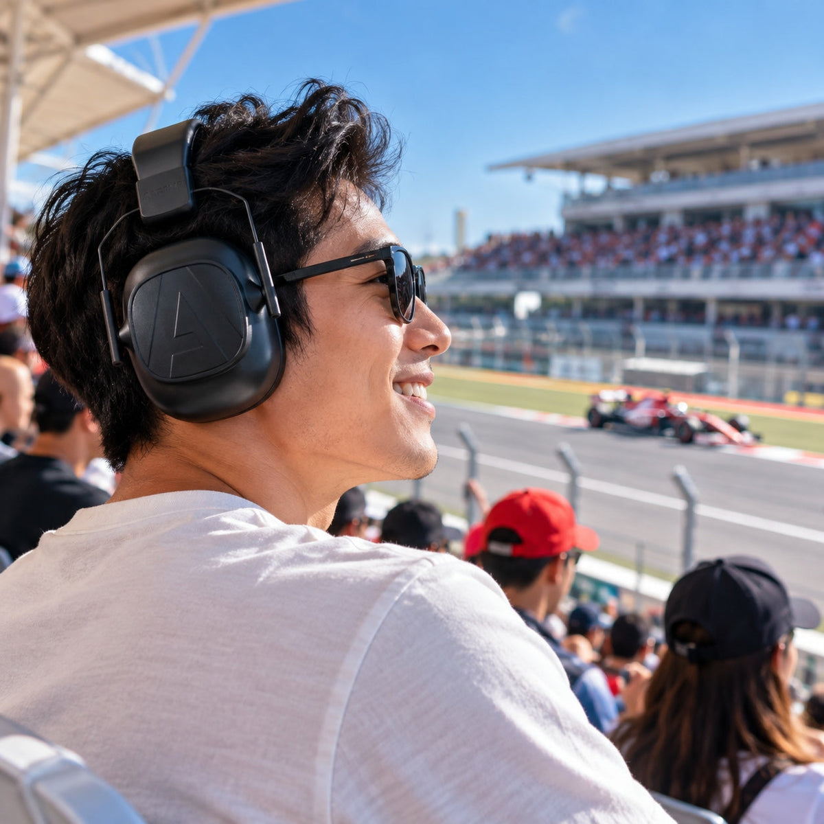 Man wearing black Alpine Defender earmuffs while watching a motorsport race from the grandstand