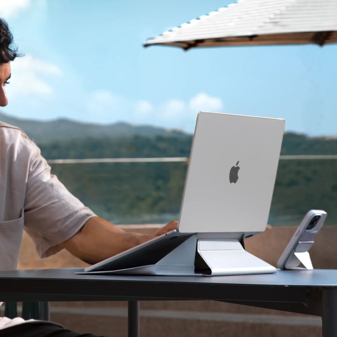 Man using the MOFT Laptop Carry Sleeve with laptop stand outdoors, showing its ergonomic design and sleek vegan leather finish