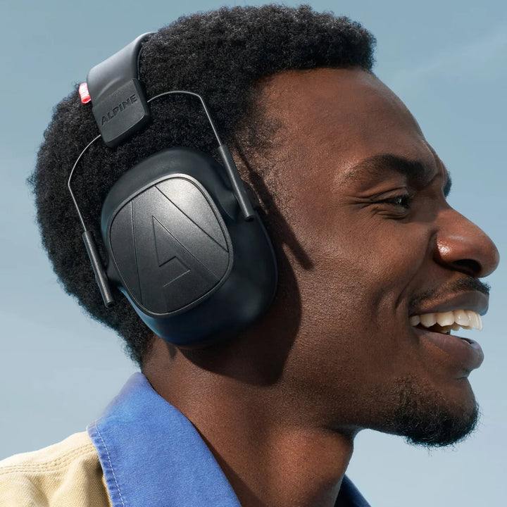 Man wearing Alpine Defender earmuffs, showcasing a comfortable fit, sleek design, and effective noise reduction outdoors.