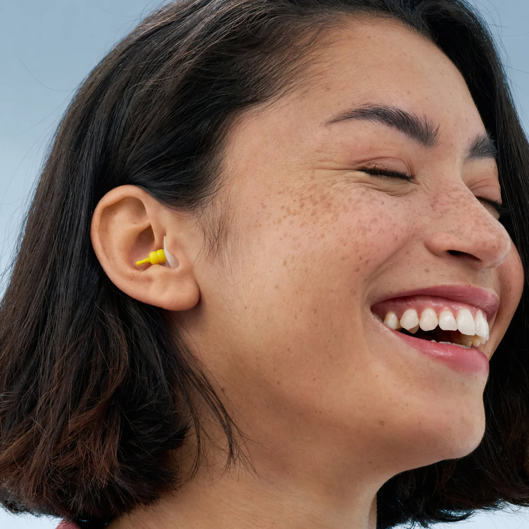 Smiling woman wearing Alpine FlyFit earplugs, showcasing a comfortable fit and effective design for air travel noise reduction.