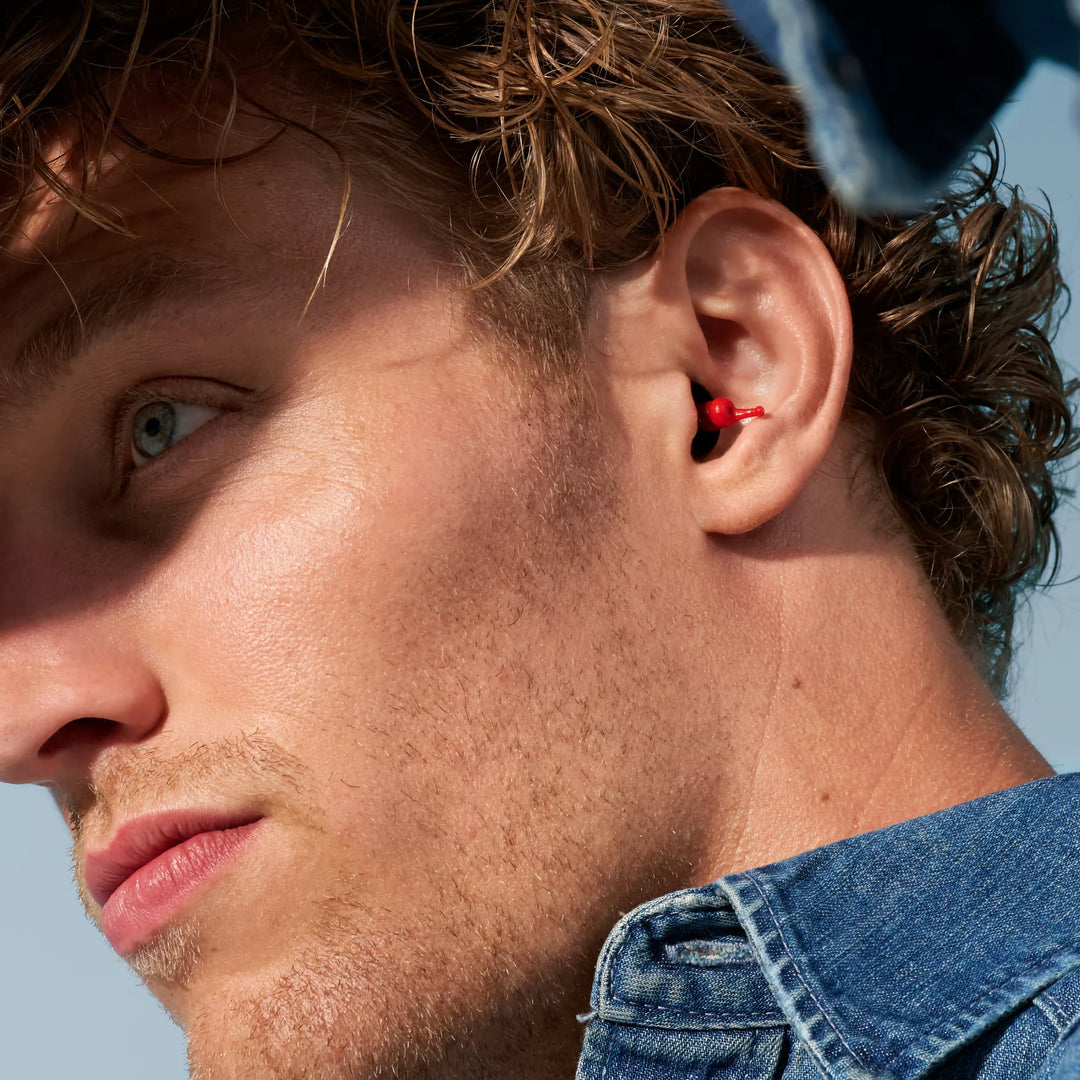 Close-up of a man wearing Alpine MotoSafe Race earplugs, highlighting the red design and snug fit in the ear.