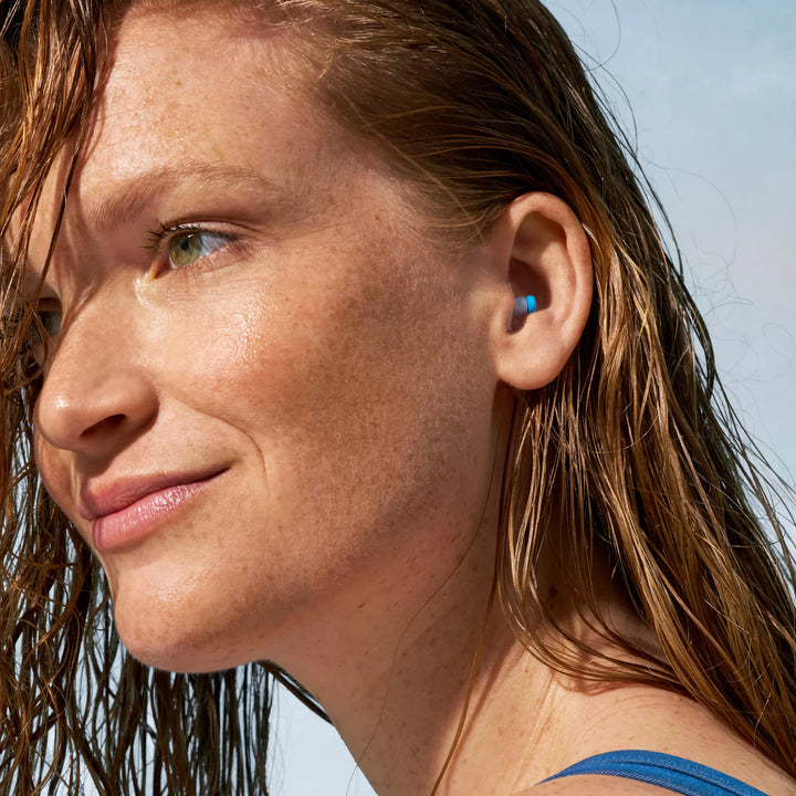 Close-up of a swimmer with wet hair wearing an Alpine SwimSafe white and blue swimming earplug