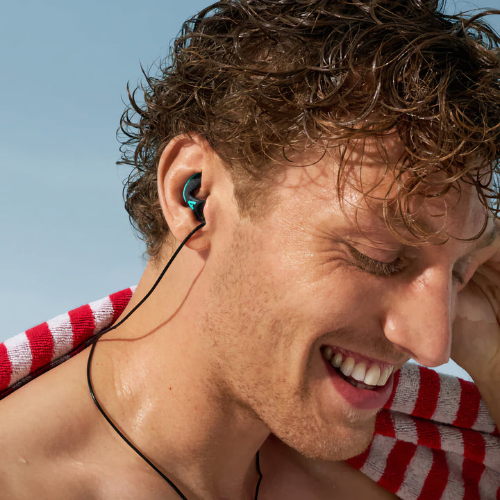 Man at the beach wearing Alpine WaterSafe Pro earplugs with a secure fit, ideal for swimming and water activities.