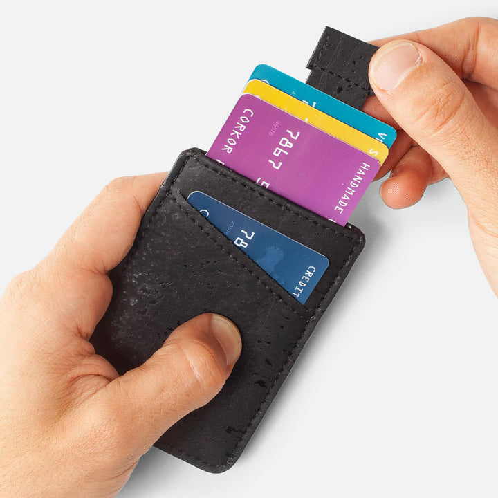 Hands using the pull-tab feature on the Corkor CK241 black vegan cork card sleeve wallet, demonstrating easy access to stored cards in a sustainable, minimalist design.