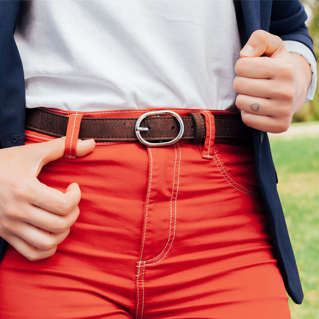 Close-up of a dark brown Corkor vegan cork belt with a silver buckle, styled with red pants and a casual white top.