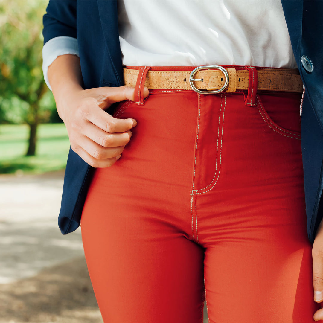 Close-up of a light brown Corkor vegan cork belt with a silver buckle, styled with red pants and a casual white top.