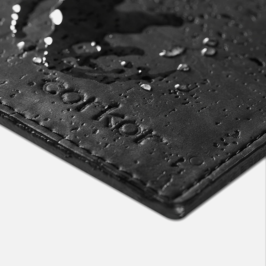 Close-up of Corkor black mouse pad with water droplets, stitched edge, and embossed logo