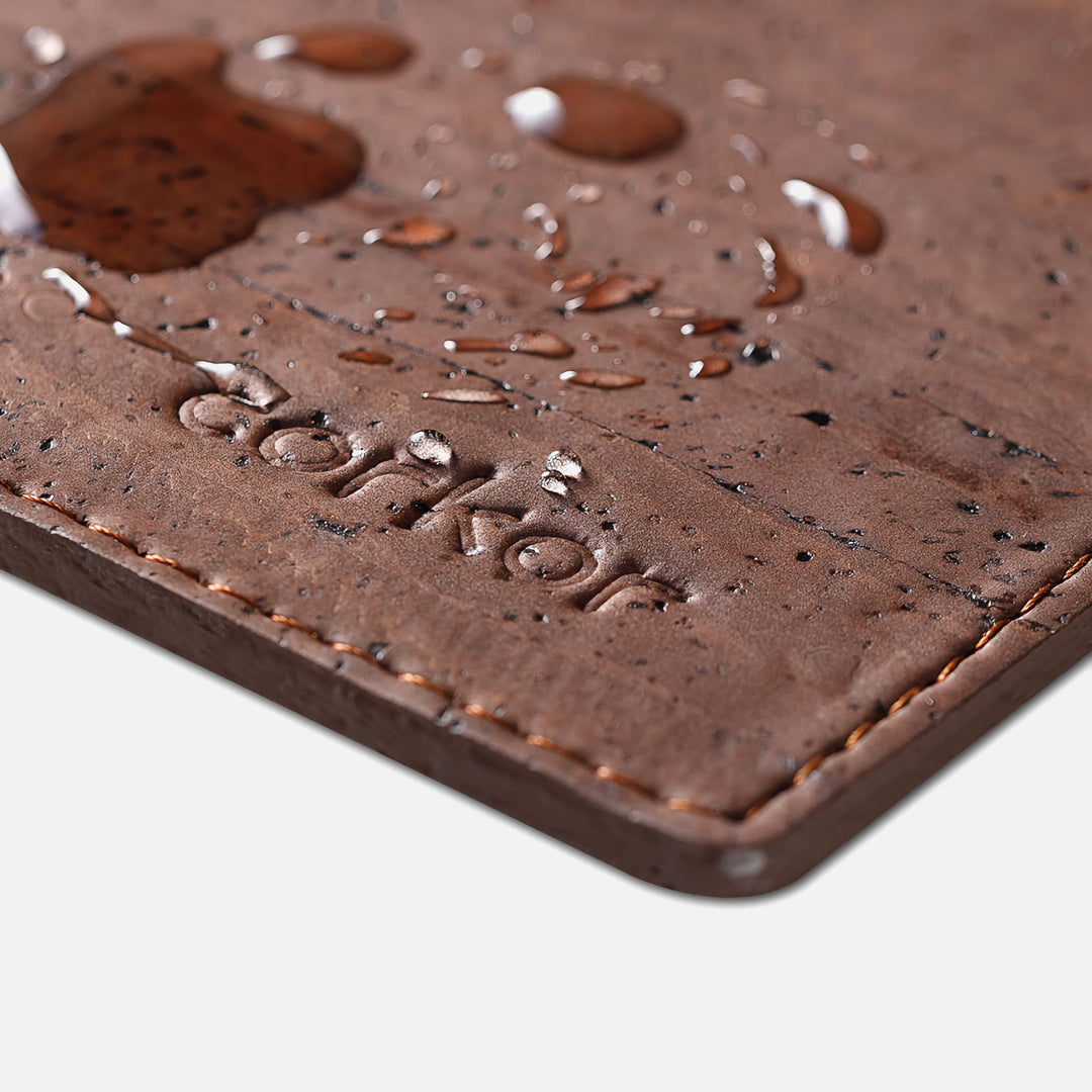 Close-up of Corkor dark brown mouse pad with water droplets, stitched edge, and embossed logo