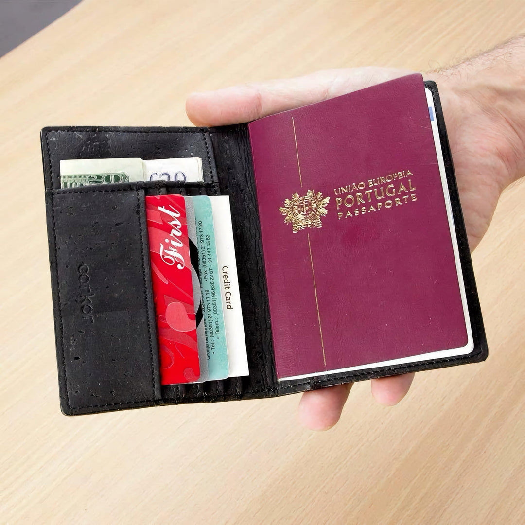 Corkor Vegan Cork Passport Wallet in black, shown in use holding passport, cards, and cash in hand