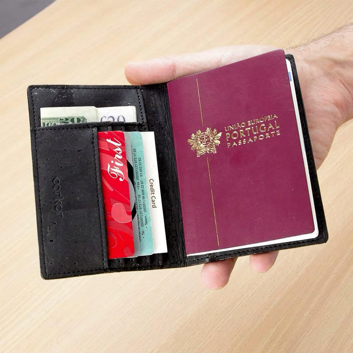 Corkor Vegan Cork Passport Wallet in black, shown in use holding passport, cards, and cash in hand