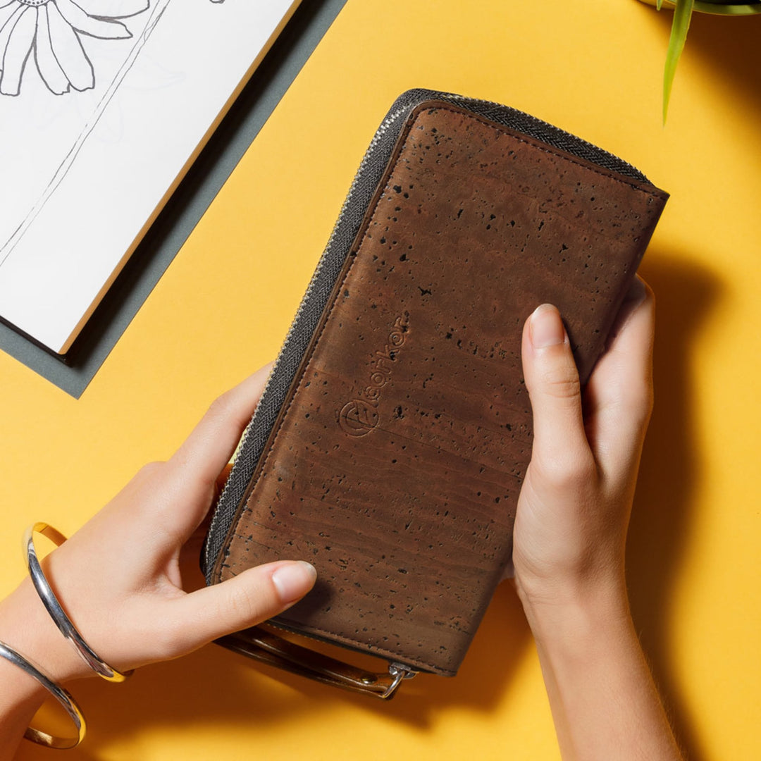 Hands holding Corkor Vegan Cork Women's Long Wallet in dark brown, highlighting its natural cork texture and elegant design.