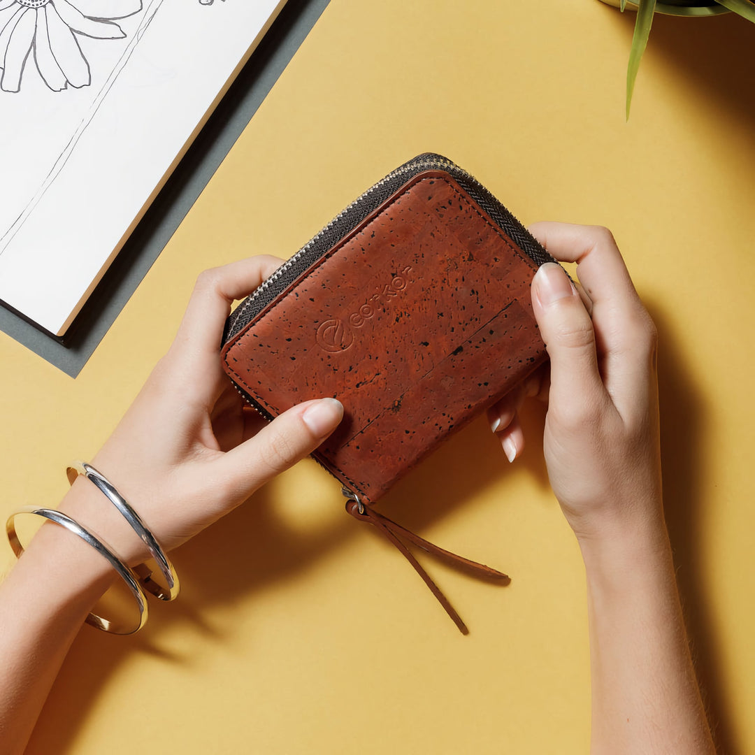 Corkor red cork square wallet held by hands on yellow desk with zip-around edge