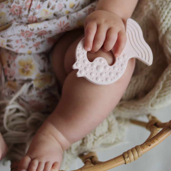 Baby holding HEVEA Fish Teether in Powder Pink, soft natural rubber teething toy with textured surface for gum relief