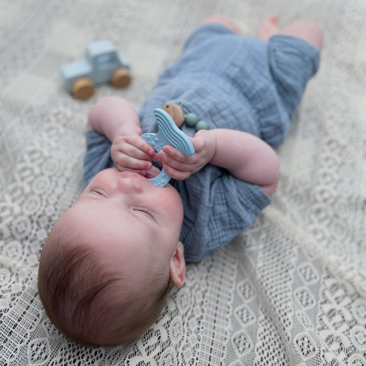 Baby lying down using HEVEA Fish Teether in Sky Blue, soft natural rubber teether with textured surface for gum relief