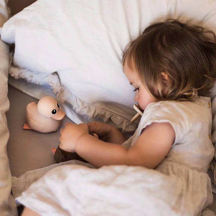 Child cuddling with HEVEA Kawan Rubber Ducks in bed, highlighting their soft, natural, and safe design for comfort and play.