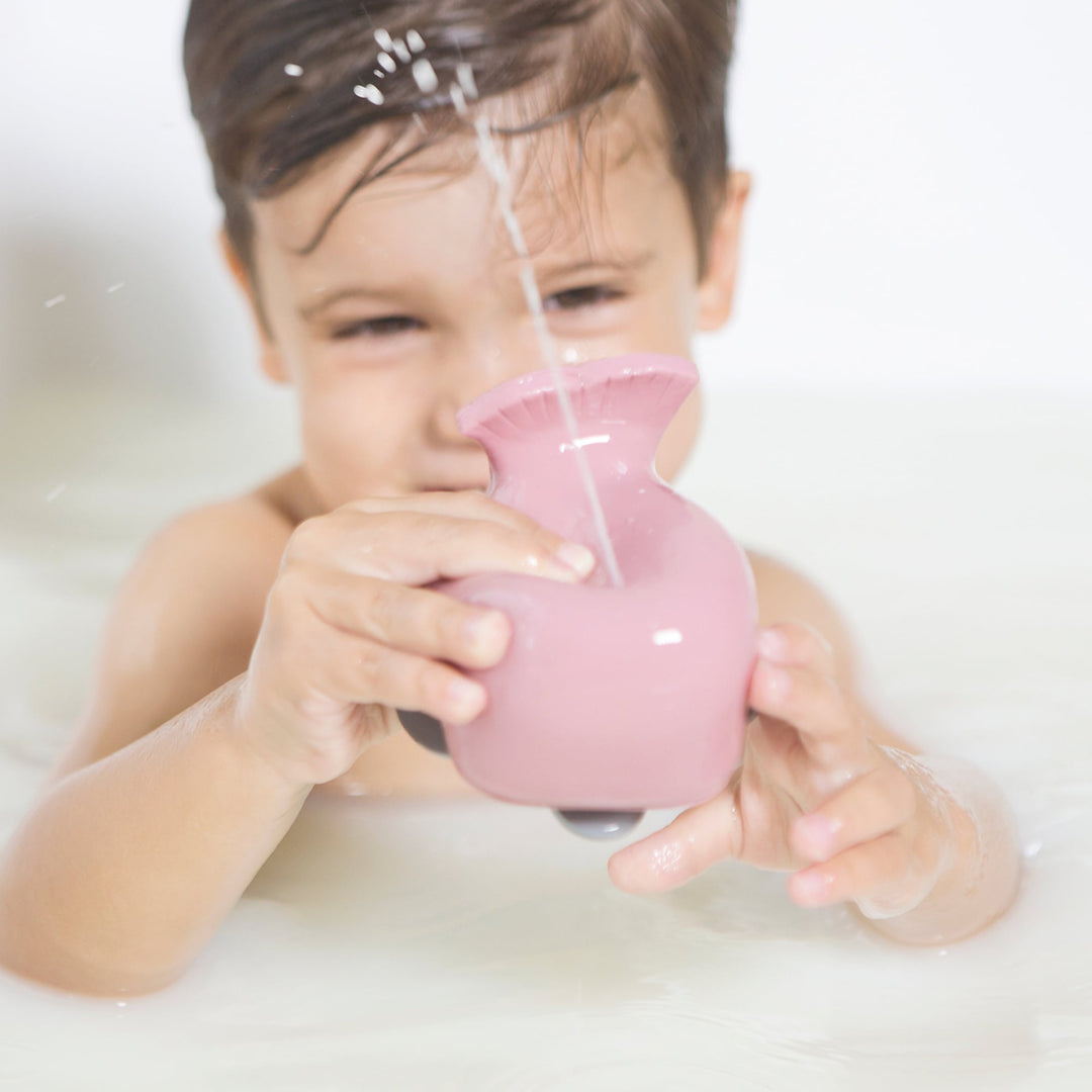 Toddler playing with HEVEA Squeeze'n'Splash Whale bath toy in Ingeborg pink, squeezing water spray in bathtub