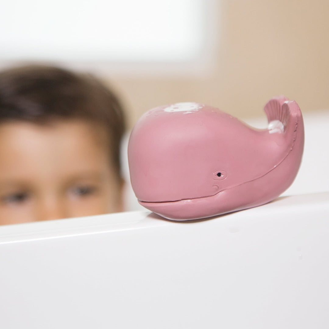 HEVEA Squeeze'n'Splash Whale bath toy in Ingeborg pink resting on tub edge, natural rubber, mould-free design