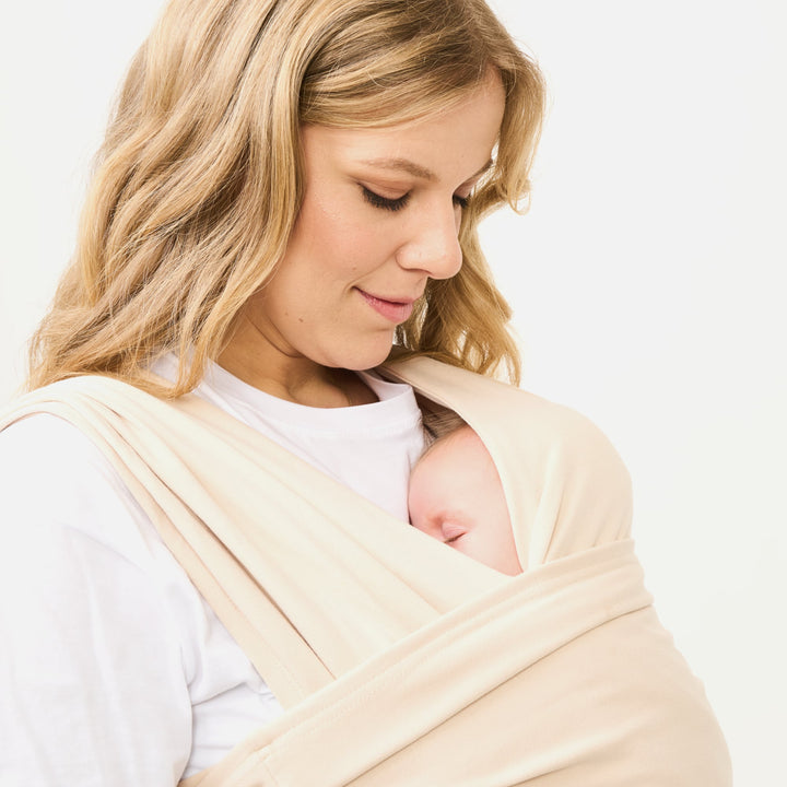 Mother wearing the Koala Cuddle Band 2 baby sling carrier in beige, gently holding her sleeping baby close for warmth and comfort.