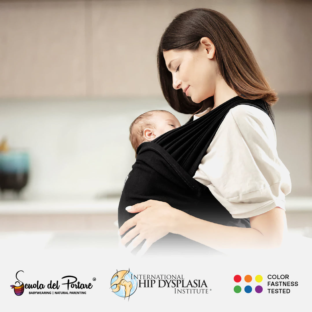 Mother wearing the Koala Cuddle Band 2 baby wrap carrier in black, holding her baby securely. Certified by the International Hip Dysplasia Institute.