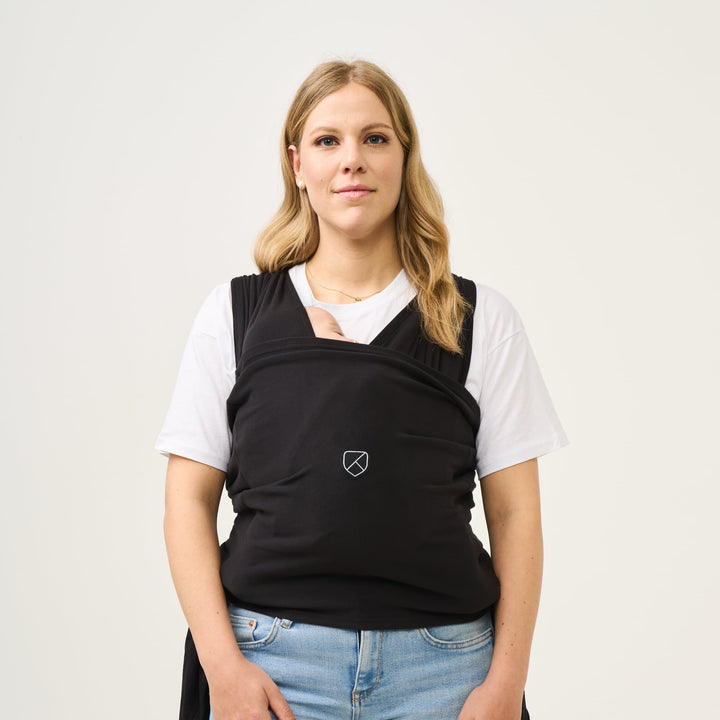 Woman wearing the Koala Cuddle Band 2 baby wrap in black, carrying a newborn in a secure and ergonomic position.