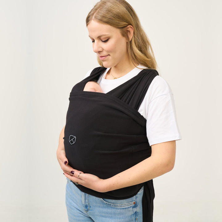 Woman gently cradling her baby while wearing the Koala Cuddle Band 2 baby wrap in black, ensuring a snug and secure fit.