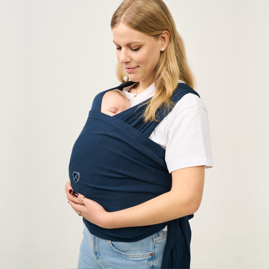 Mother wearing Koala Cuddle Band 2 in dark blue while baby sleeps peacefully in front-carry position