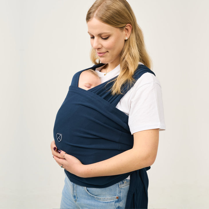 Mother wearing Koala Cuddle Band 2 in dark blue while baby sleeps peacefully in front-carry position