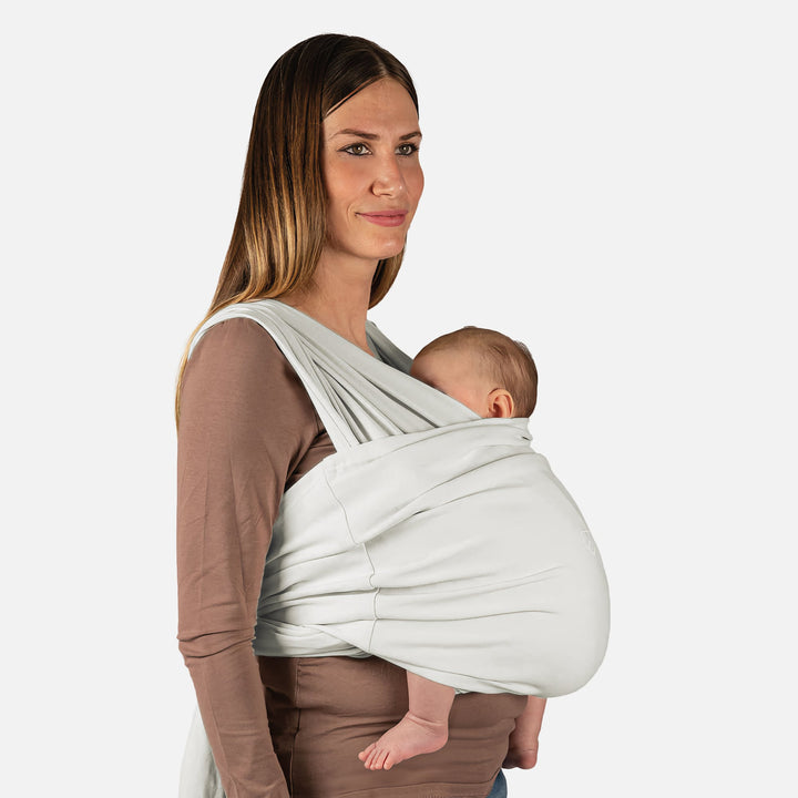 Side view of a mother wearing the Koala Babycare Koala Cuddle Band 2 gray baby sling carrier, holding her baby securely for hands-free comfort.