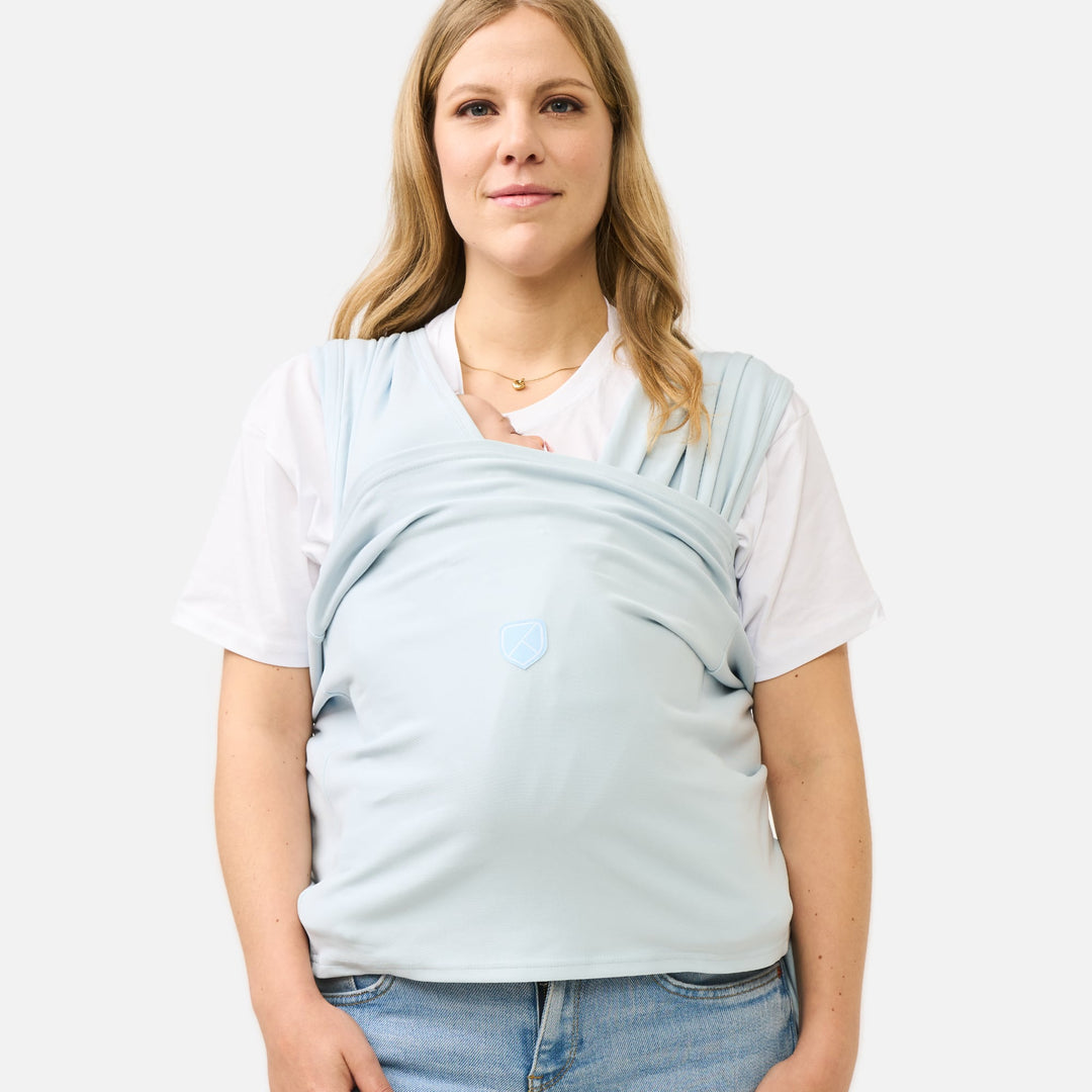 Woman wearing the Koala Cuddle Band 2 baby wrap in pastel light blue, securely carrying her baby for hands-free comfort.