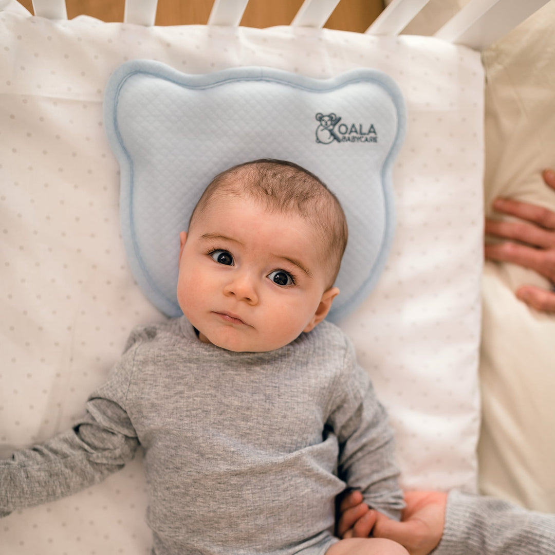 Infant lying on the Koala Babycare Koala Perfect Head pillow in light blue, providing ergonomic support for head and neck in a crib.