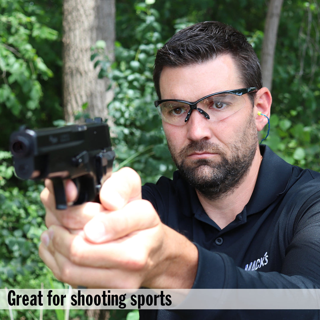 Man wearing Mack's Ear Seals earplugs and safety glasses while shooting a handgun outdoors, demonstrating noise protection for shooting sports.