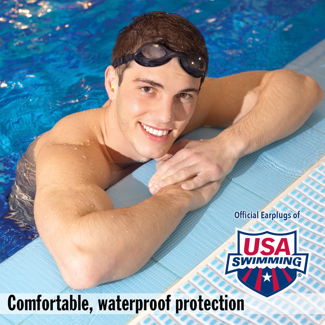 Smiling man in a swimming pool wearing Mack's Ear Seals earplugs, providing comfortable waterproof protection. Official earplugs of USA Swimming.