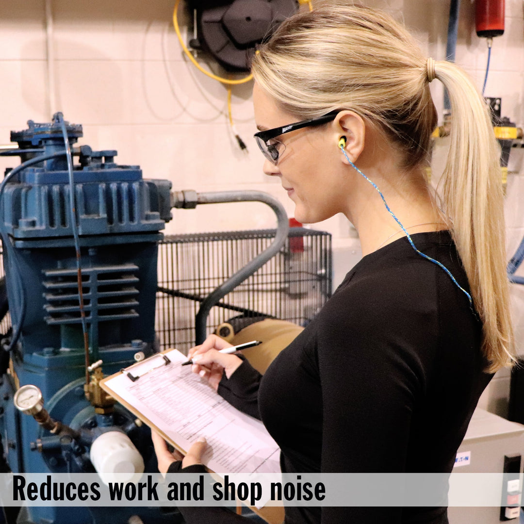 Woman wearing Mack's Ear Seals earplugs in a noisy industrial workplace, using a clipboard while reducing work and shop noise.