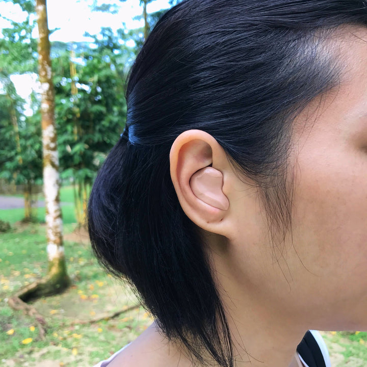 Woman wearing Mack's Silicone Earplugs outdoors, showcasing a secure and custom fit for noise and water protection.